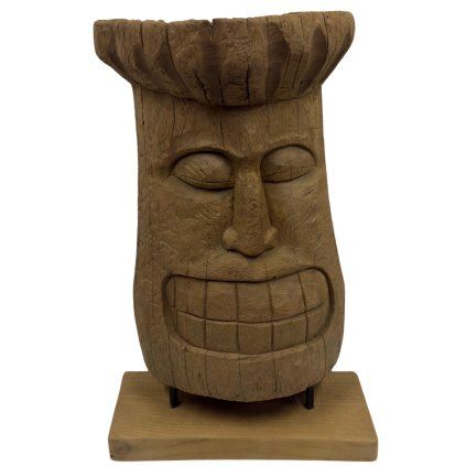 Tiki totem v podobě hlavy, precizně vyřezaný z teakového dřeva, umístěný na podstavci.