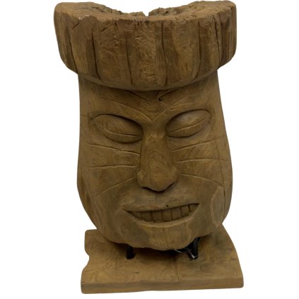 Tiki totem v podobě hlavy, precizně vyřezaný z teakového dřeva, umístěný na podstavci.